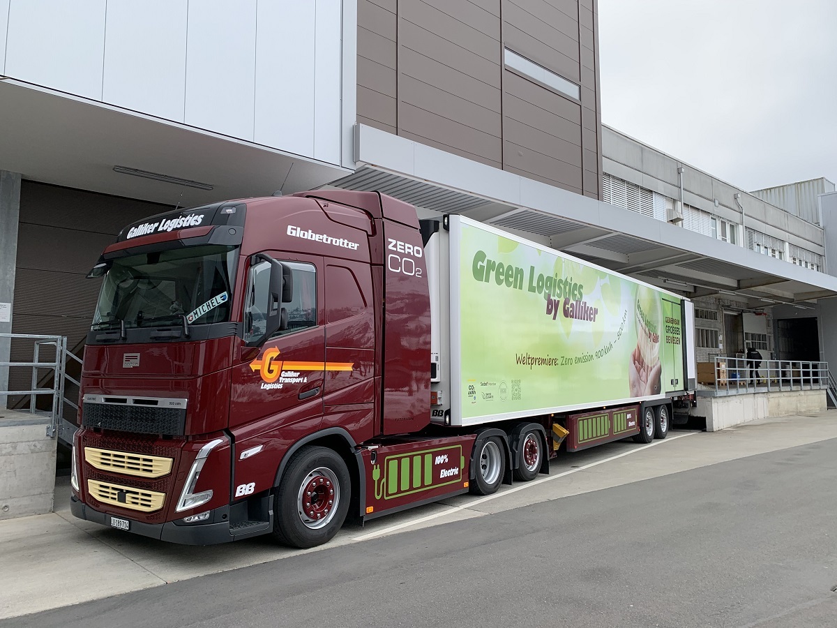 Elektryczne ciężarówki ładują ekologiczne paczki przed magazynem z panelami słonecznymi